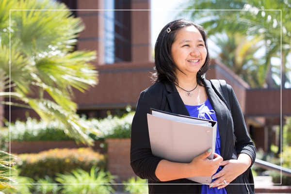 Woman walking outside a campus building holding a binder