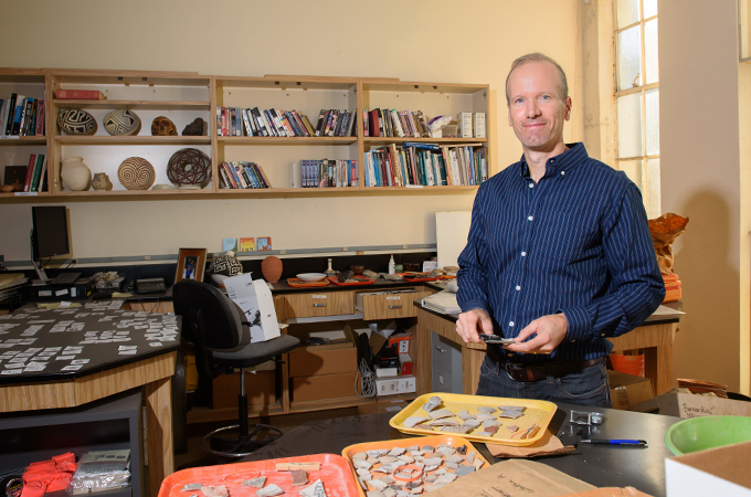 Professor Bernardini stands in his office with artifacts on display.