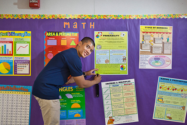 Man leans over a poster and staples it to a wall in a classroom