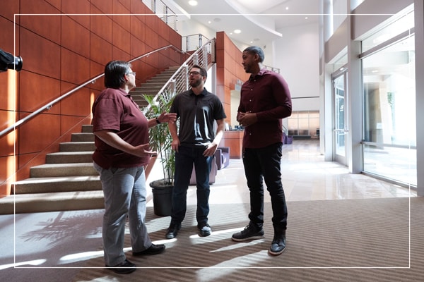 Faculty member speaking with two students in a hallway