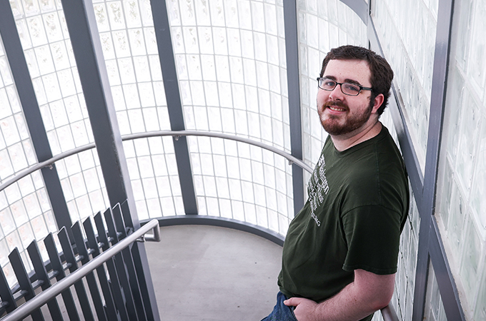 Jacob Griffin leans against a wall of glass tiles in a stairwell.