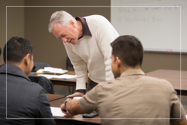 A professor helping two students at their desk