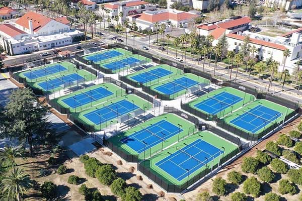 Overhead image of Verdieck Tennis Courts. The courts are blue surrounded by green pavement. university buildings and orange groves surround the complex.