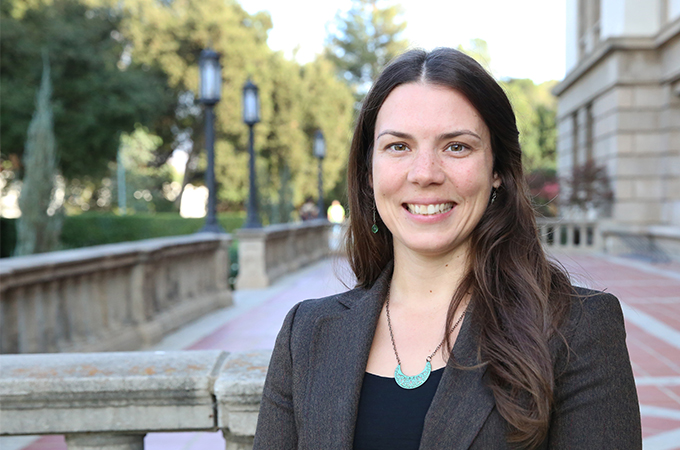 A woman in a grey blazer smiles and stands outside near the hall of letters.