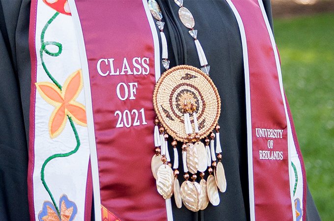 A student pairs a traditional Native American necklace with their Class of 2021 Commencement sash.